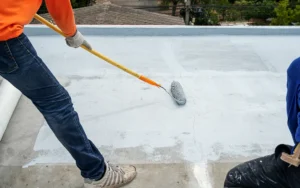 A contractor applying a waterproofing sealant with a roller in Long Island, NY.